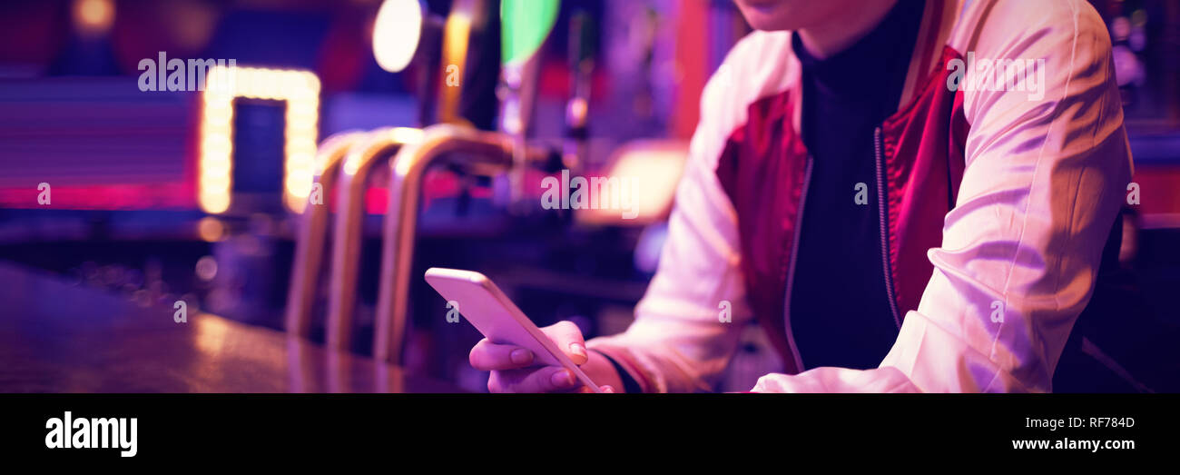 Female bartender using mobile phone at bar counter Stock Photo