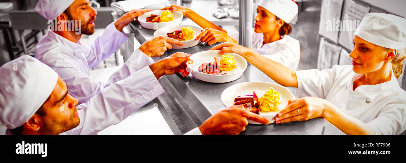 Chefs passing ready food to waiter at order station Stock Photo