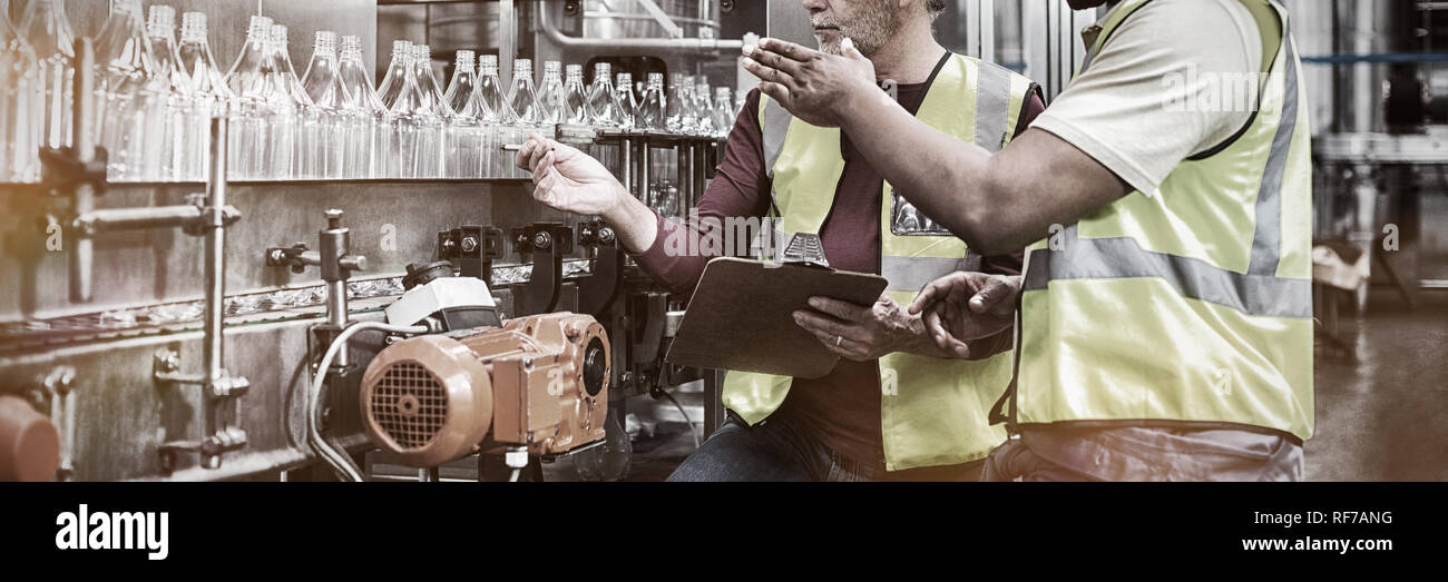 Two factory workers discussing while monitoring drinks production line Stock Photo