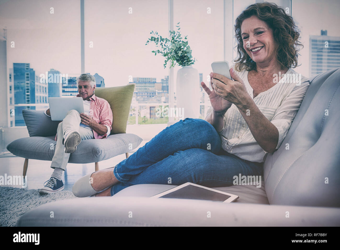Smiling woman using smartphone by man sitting at home Stock Photo