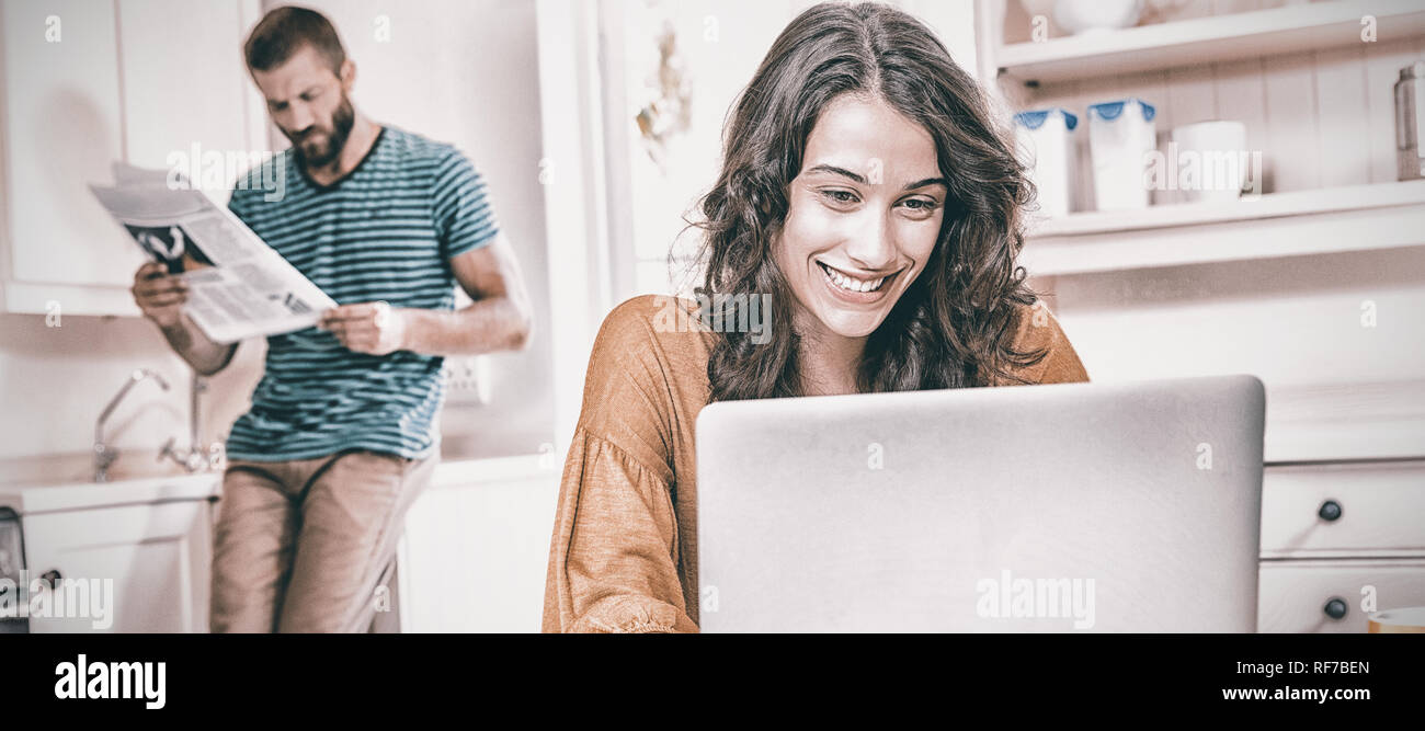 Woman using laptop while man reading newspaper in background Stock Photo
