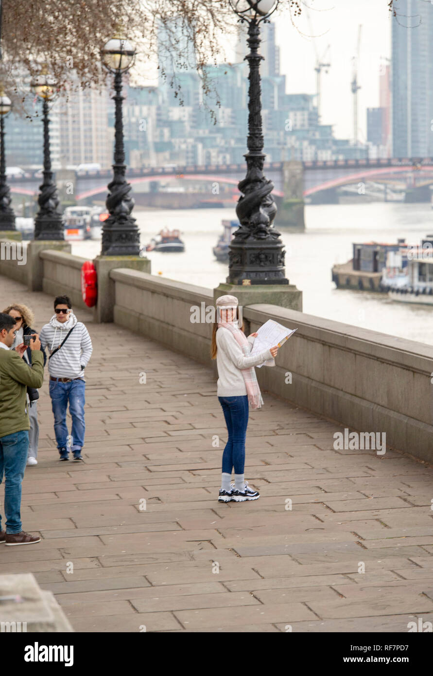 Young female tourist looking at a map being photographed by friend on the South Bank by The River Thames in London UK Stock Photo