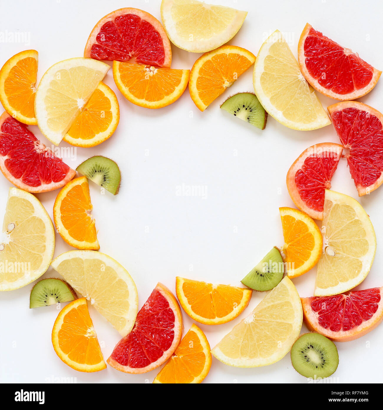 Flat lay of sliced fruits - kiwi, orange and grapefruits - arranged in a circle, copy space in the middle Stock Photo