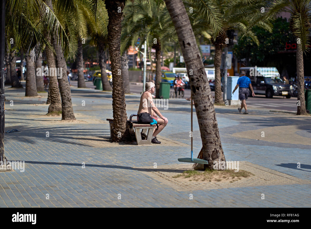 Shirtless elderly man sitting alone outside on a street bench. Pattaya, Thailand, Southeast Asia Stock Photo