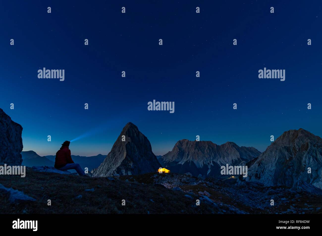 Summit of the Sonnenspitze with mountaineer and tent and Zugspitze in the background at blue hour, Ehrwald, Außerfern, Tyrol Stock Photo