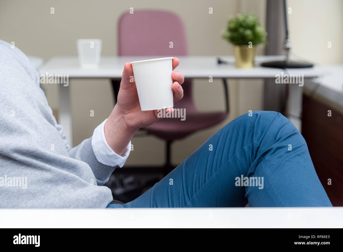 Businessman sitting at office desk and having a coffee break while holding a coffee mug in an office environment Stock Photo