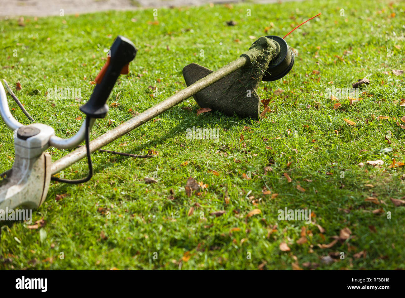 Brushcutter mower lying on green grass. Seasonal garden cleaning moder