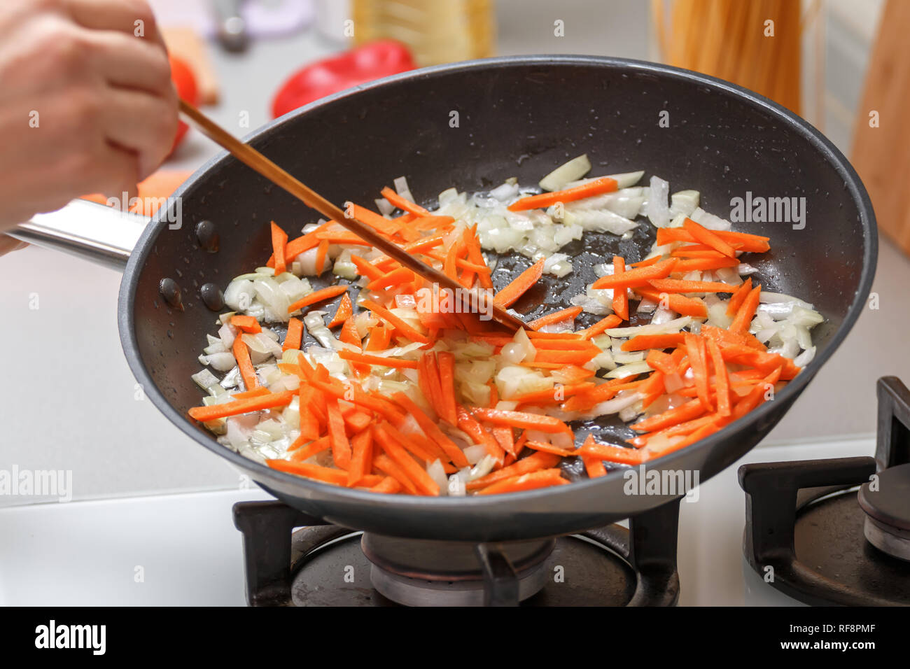 Homemade cooking. A woman fries onions and carrots in a hot frying pan with vegetable oil. Close-up. Stock Photo