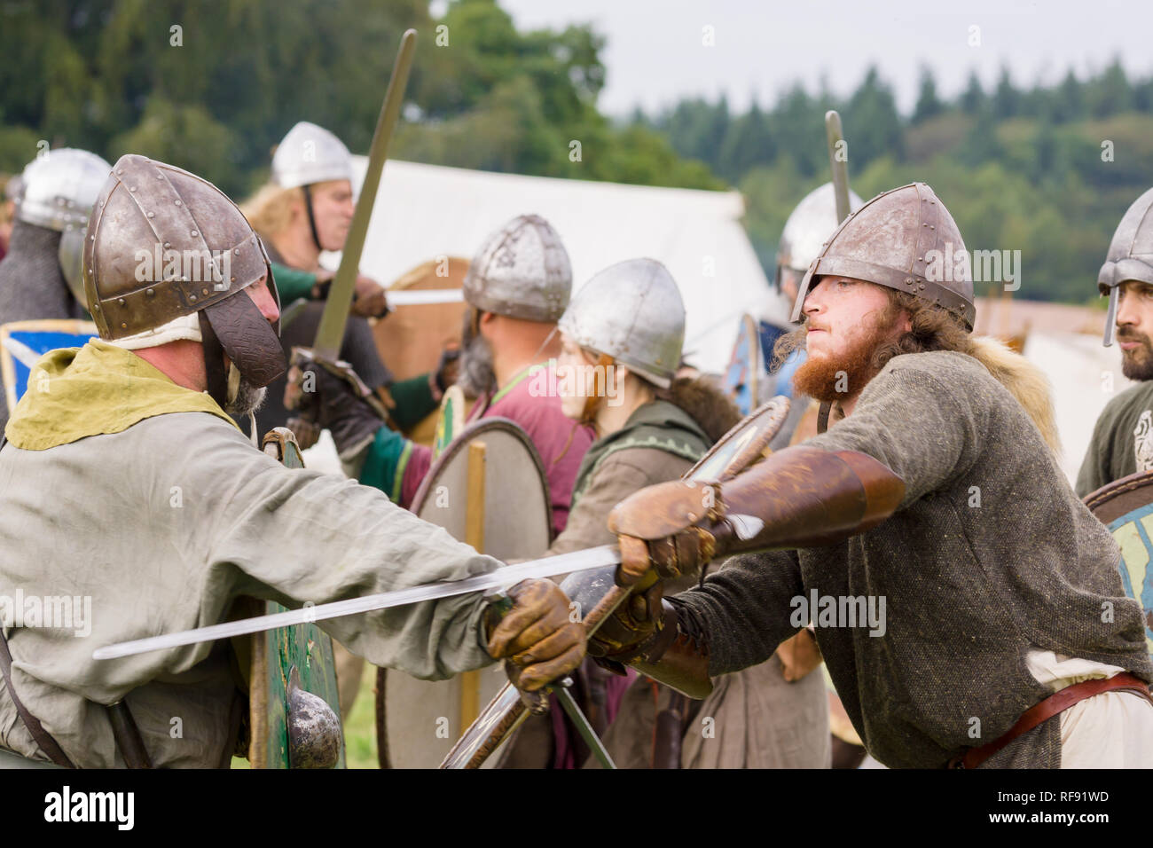 Medieval re-enactors dressed in armour and costumes of the 12th century equipped with swords and shields re-enacting combat of the period Stock Photo