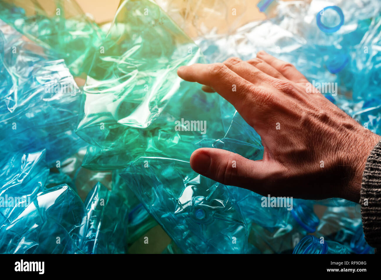 Hand among crushed plastic bottles, environmental damage concept Stock