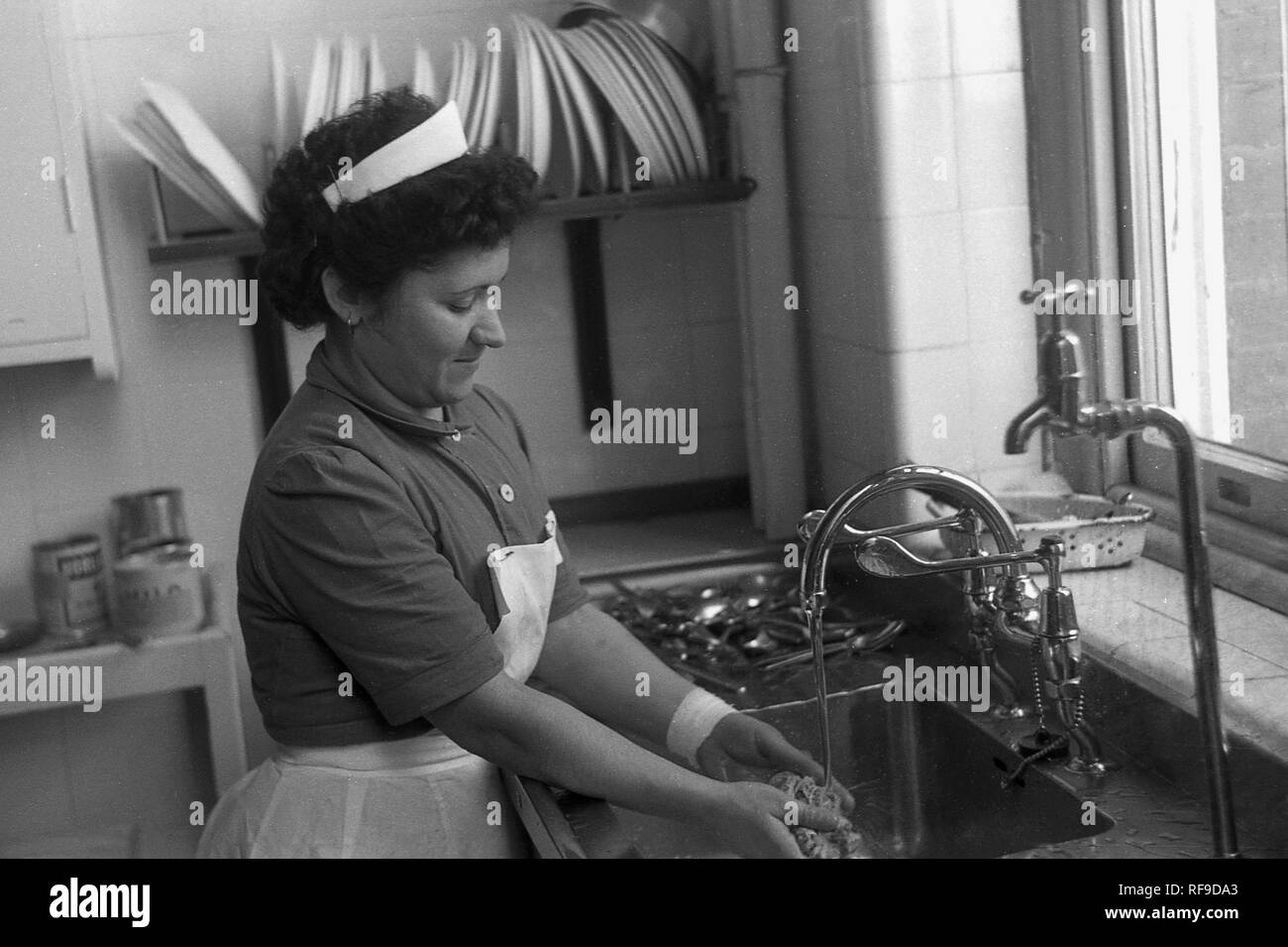 1950s, historical, a female uniformed staff nurse at a hospital kitchen sink washing a cloth, England, UK. Stock Photo