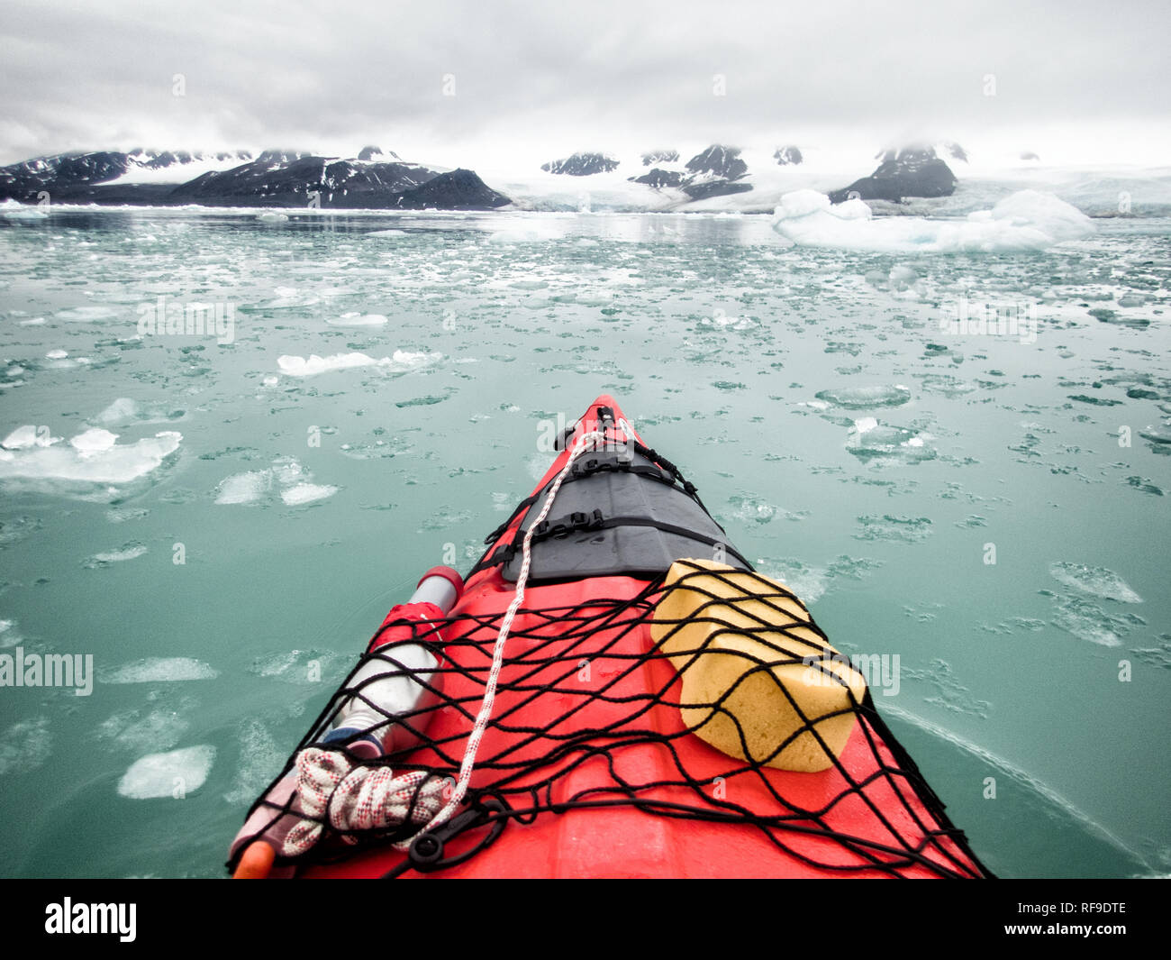 Kayaking Arctic Ice Svalbard Norway // SVALBARD, Norway — Kayaking tourists explore the icy waters and pristine landscapes of the Arctic region surrounding Svalbard. This unique and adventurous form of tourism offers an up-close experience with the Arctic environment, showcasing the region's breathtaking beauty and fragile ecosystems. Stock Photo