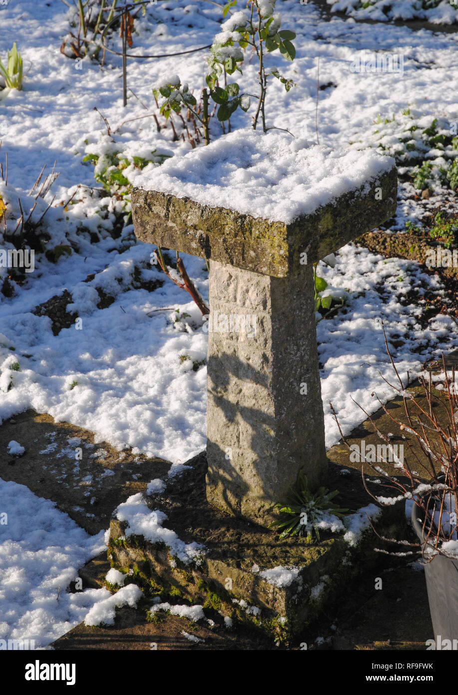 A stone bird bath with winter snow and sunshine in a UK garden Stock Photo