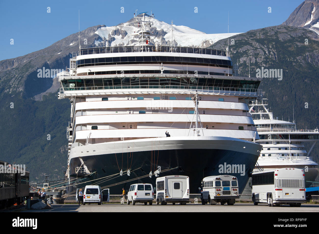 The morning view of land transportation next to giant cruise liner moored in Skagway town (Alaska). Stock Photo