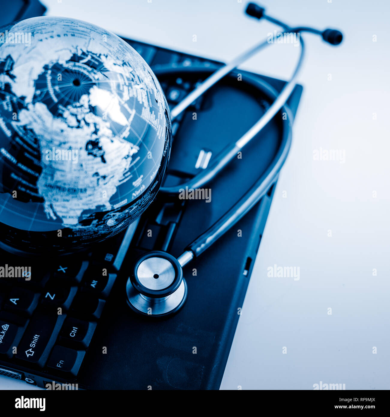 Glass globe and stethoscope on a computer keyboard.blue toned images ...