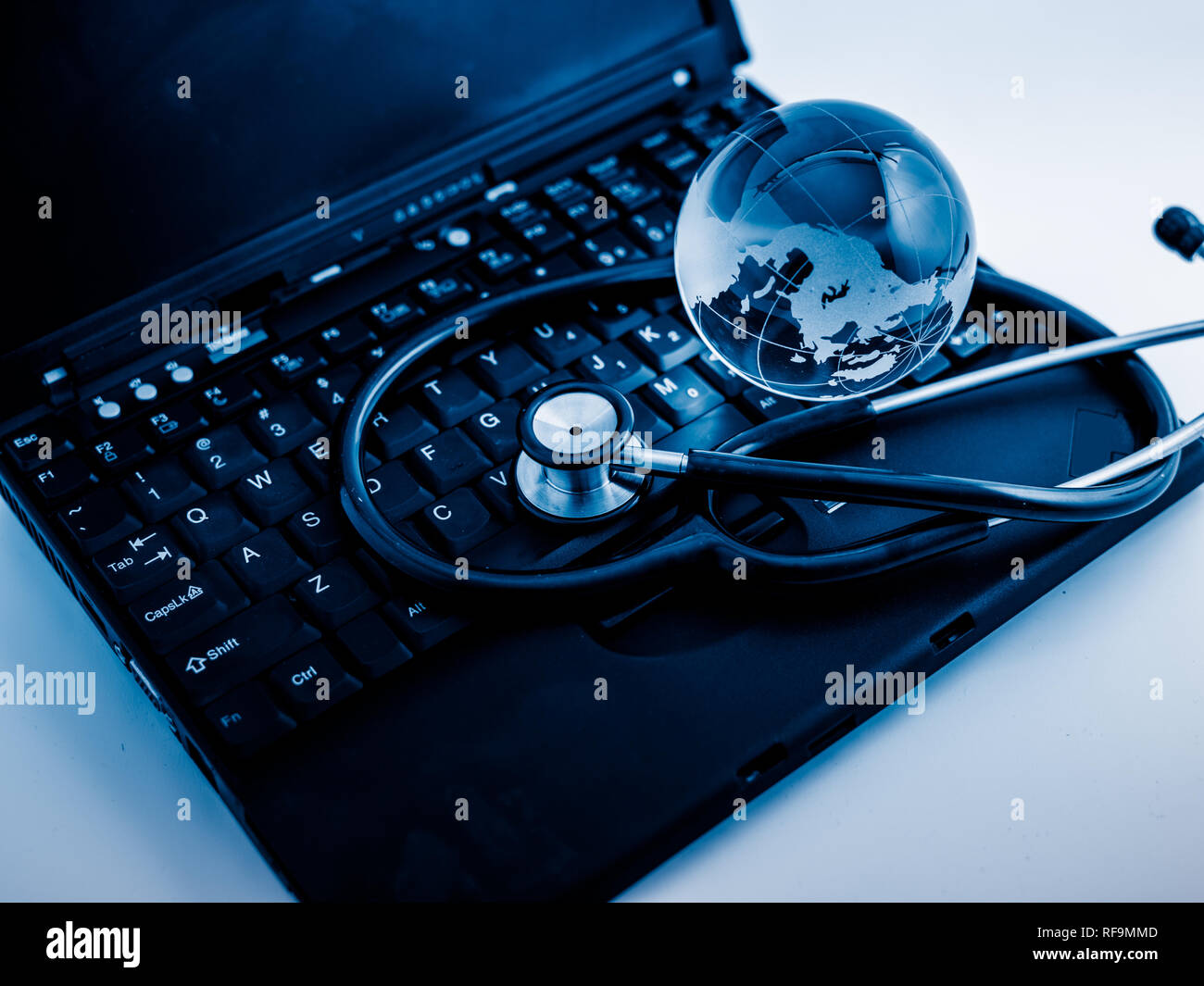 Glass globe and stethoscope on a computer keyboard.blue toned images ...