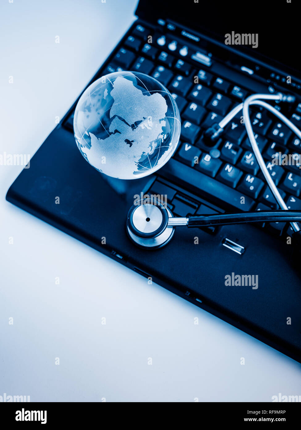 Glass globe and stethoscope on a computer keyboard.blue toned images ...