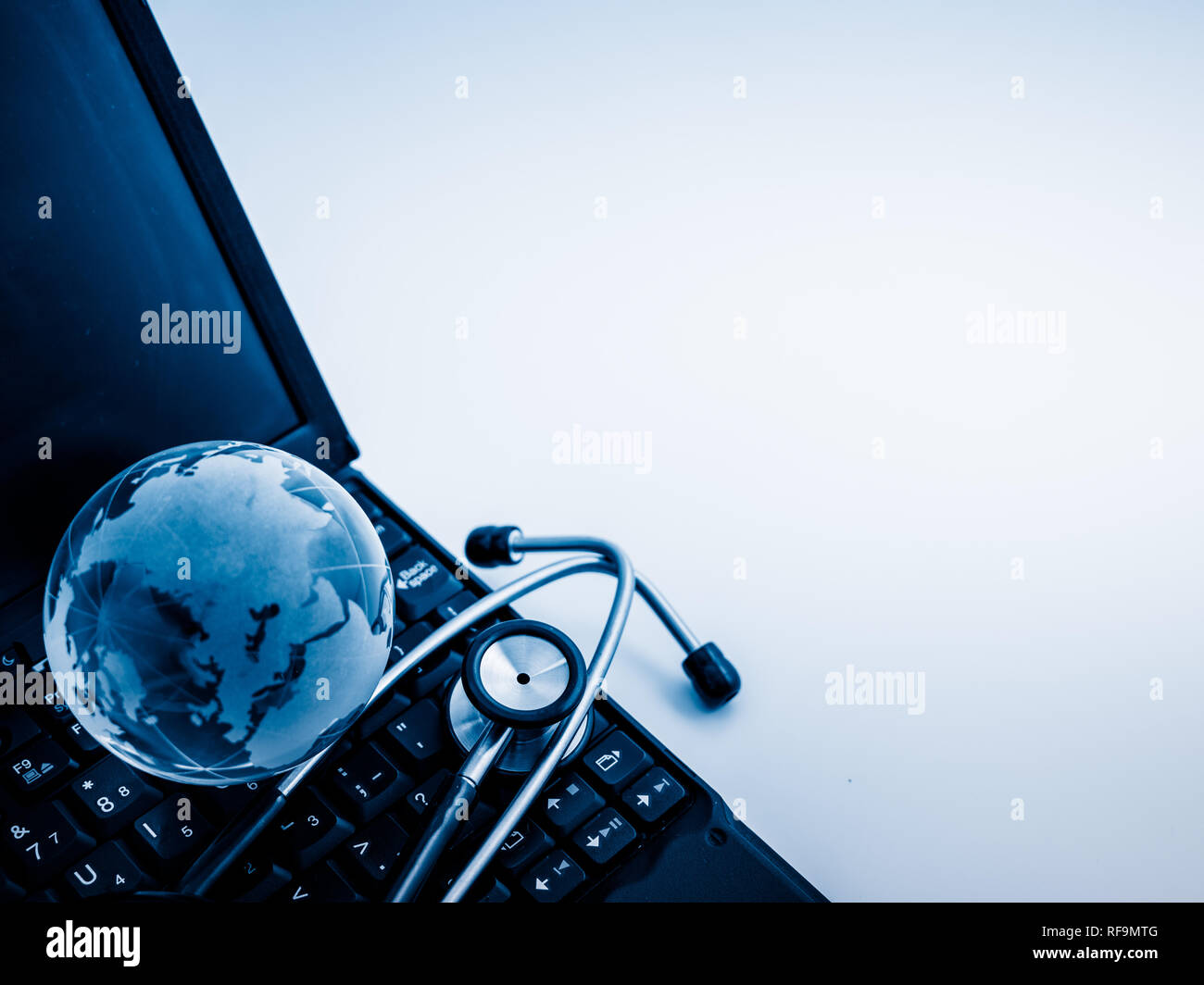Glass globe and stethoscope on a computer keyboard.blue toned images ...