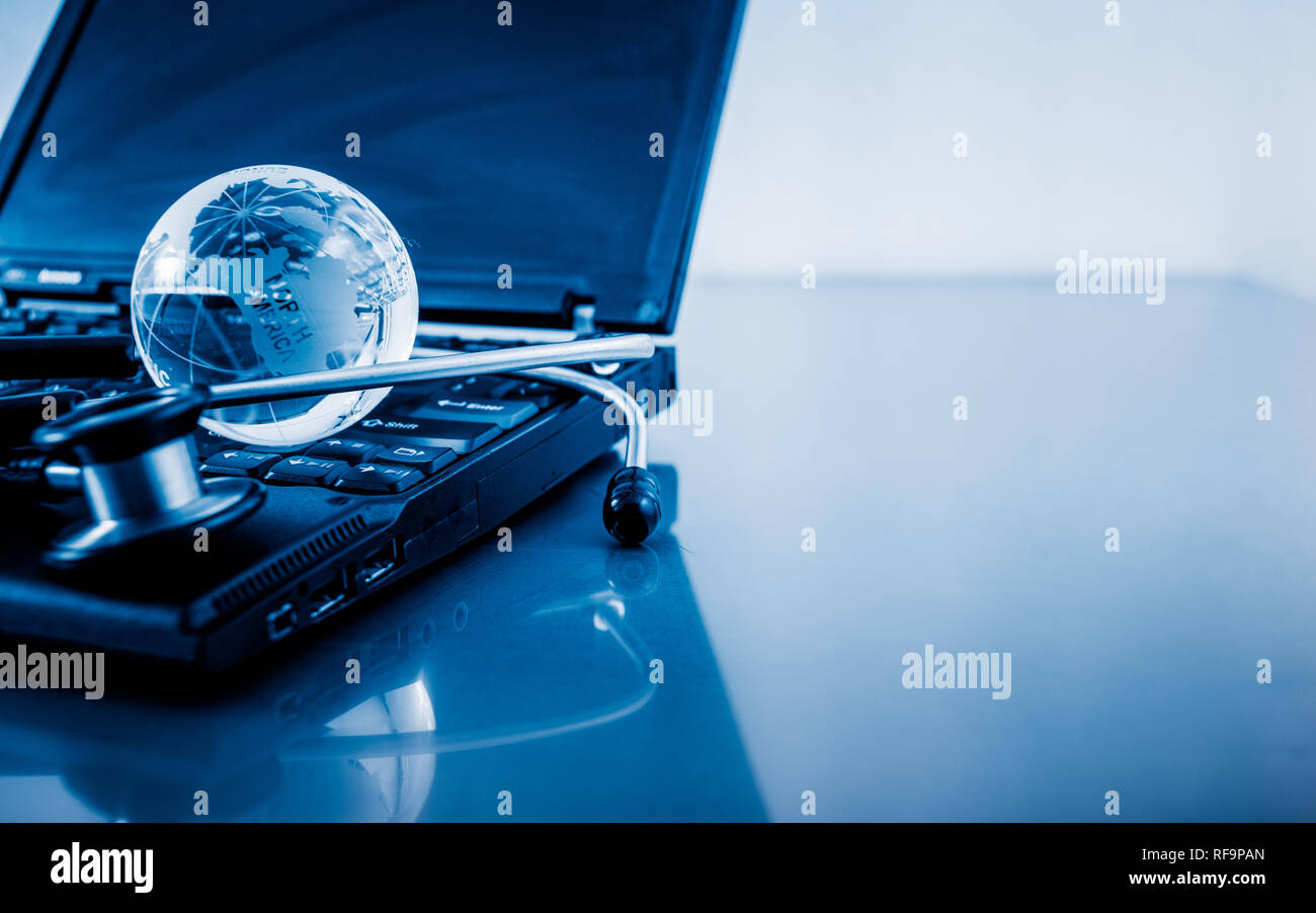 Glass globe and stethoscope on a computer keyboard.blue toned images ...