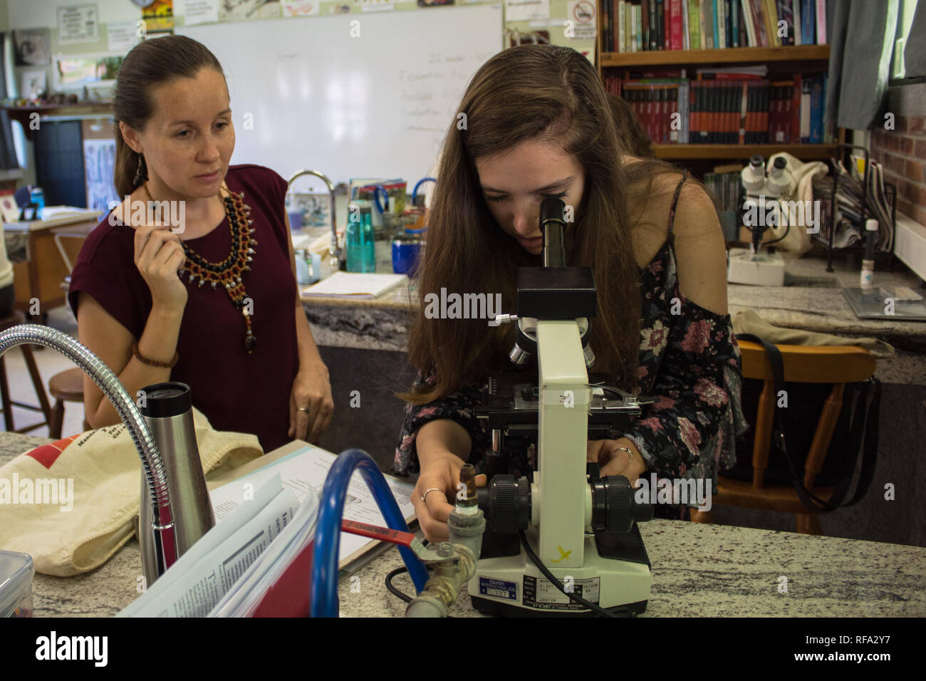 A female biology teacher observing an international student looking through microscope in a science class. Stock Photo