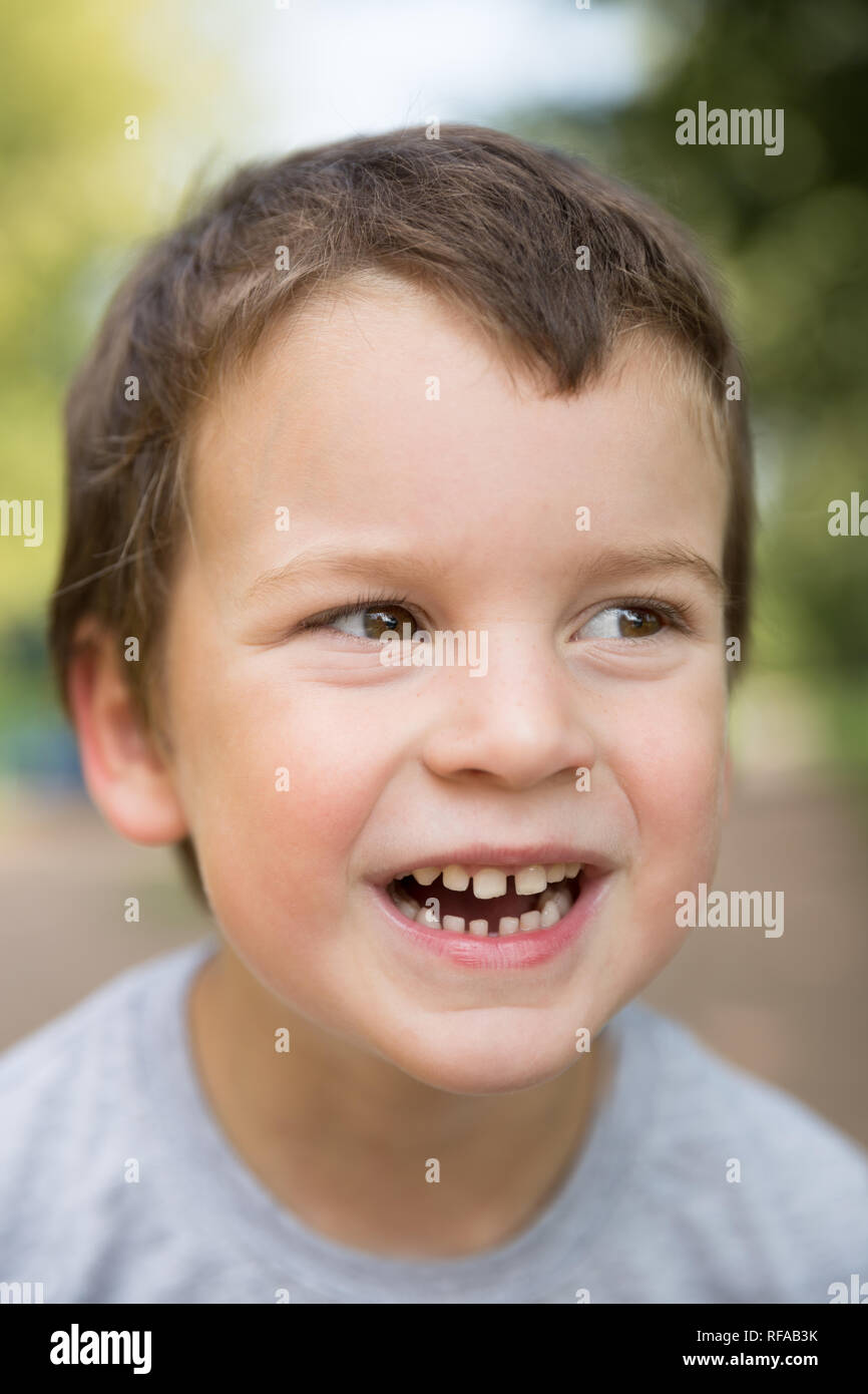 Outdoors closeup portrait of laughing freckled boy with dark hair and brown eyes Stock Photo