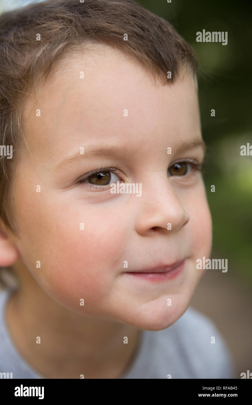 Outdoors closeup portrait of a smiling freckled boy with dark hair and