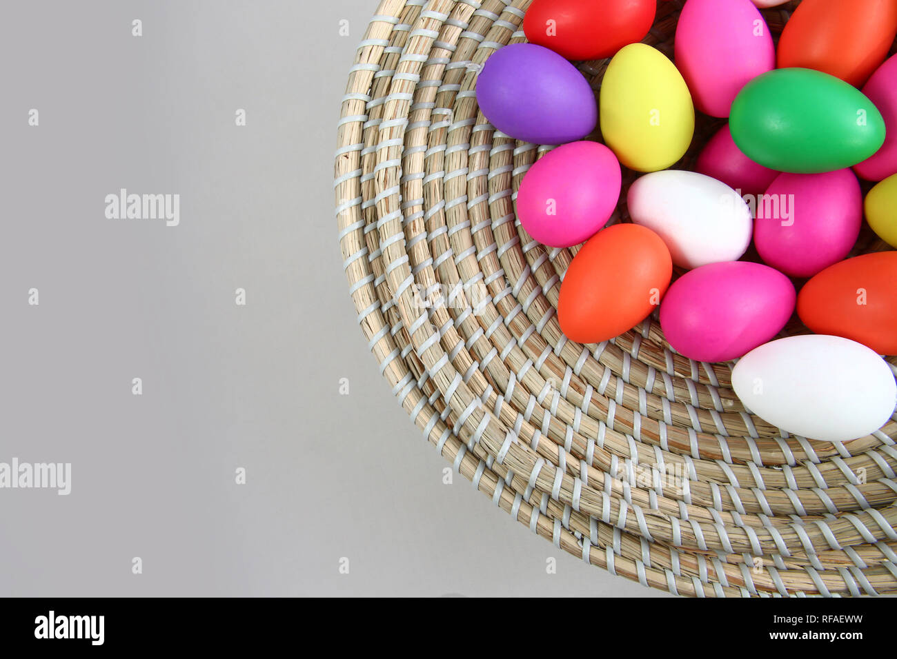 Brightly colored easter eggs, in a straw basket against a grey background. Stock Photo