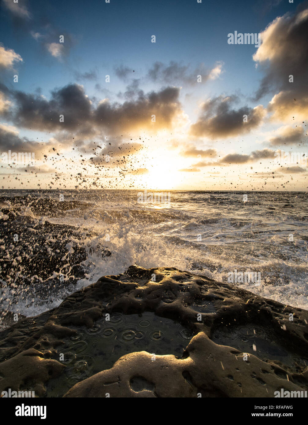 Waves crashing on a rocky beach at sunset Stock Photo