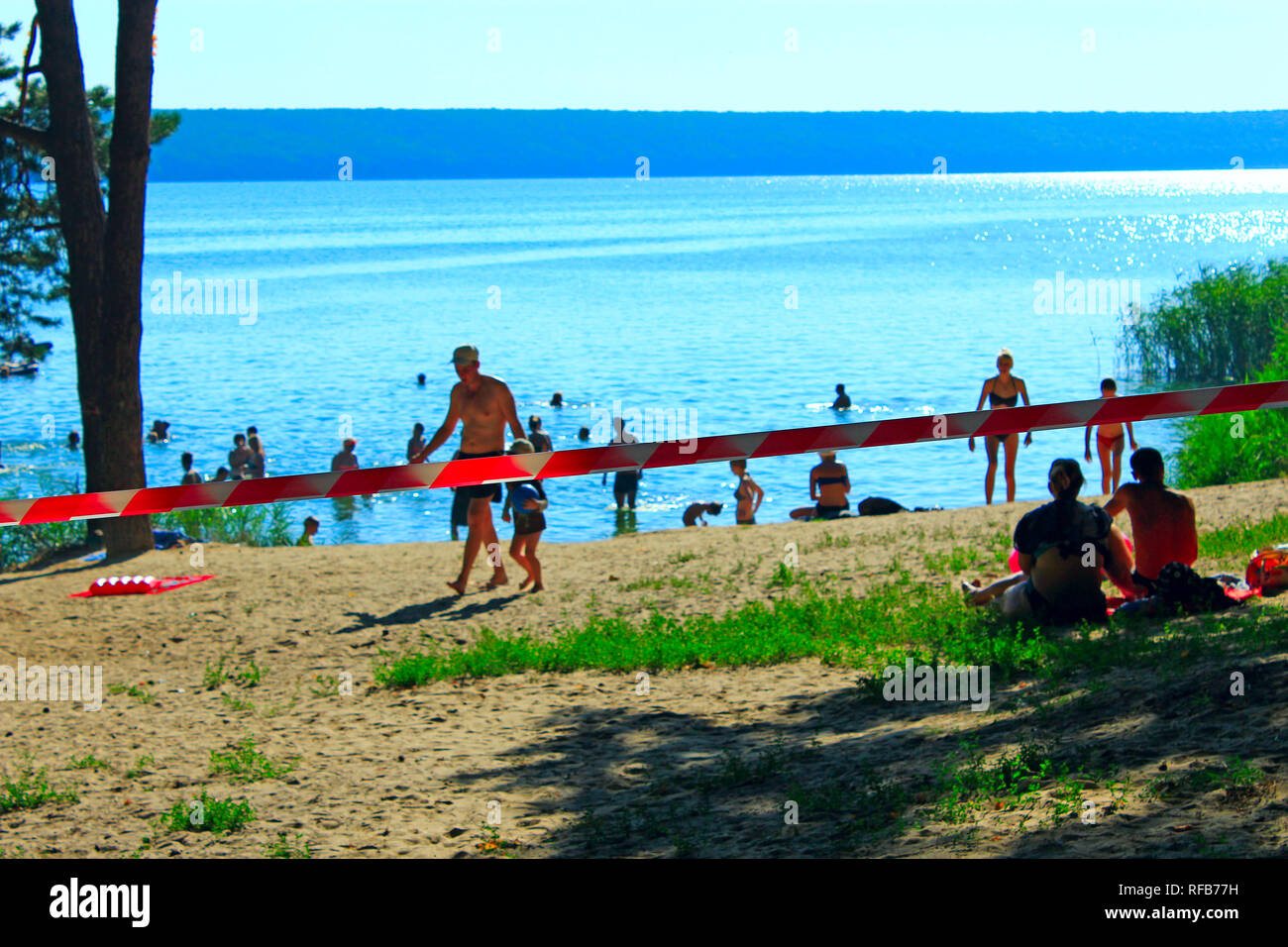People bathe in lake and sunbathe in restricted area. Territory enclosed by ribbon forbidding entrance. People ignore ban on bathing in Pechenizhskoye Stock Photo