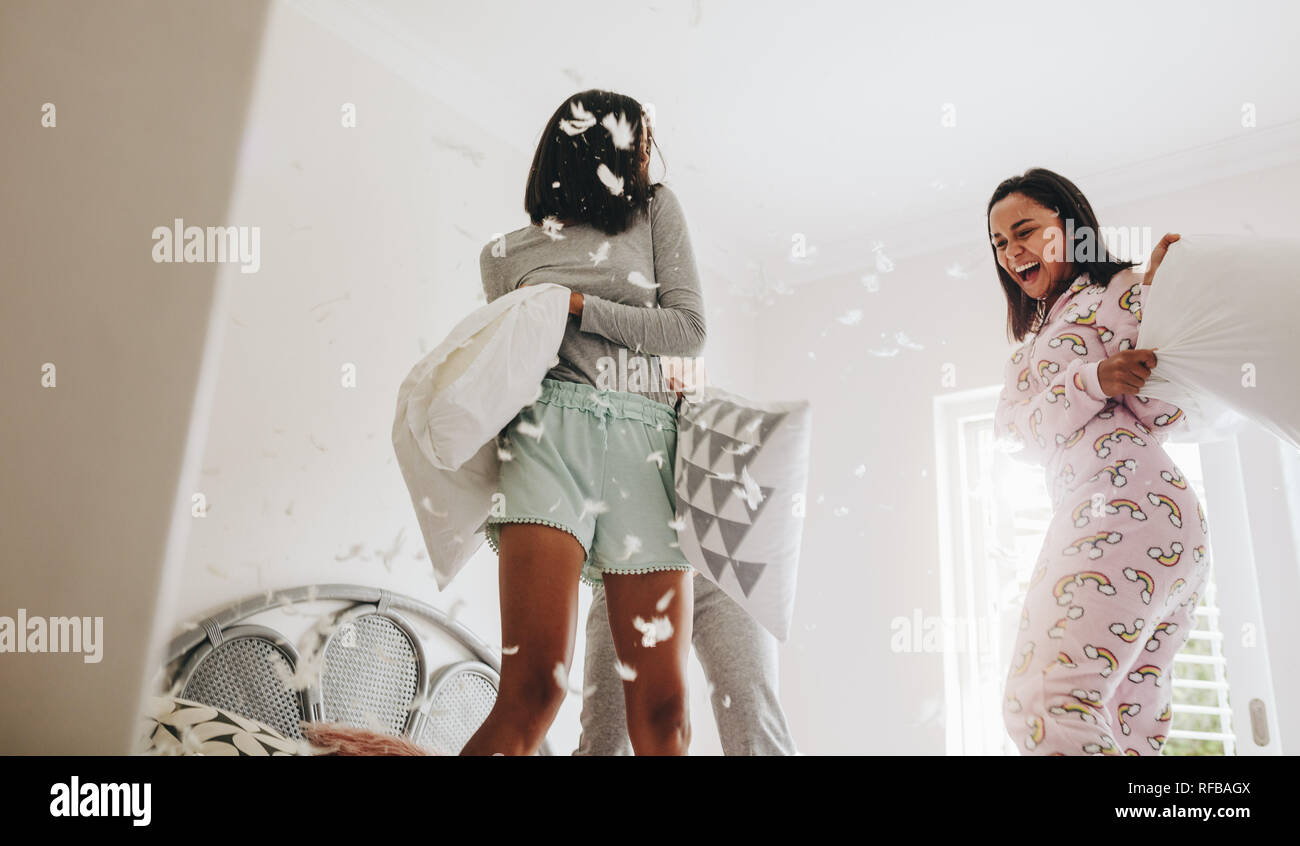 Young girls pillow fighting standing on bed. Girls having fun playing with  pillows at a sleepover with feathers flying around Stock Photo - Alamy, image size:1300x846