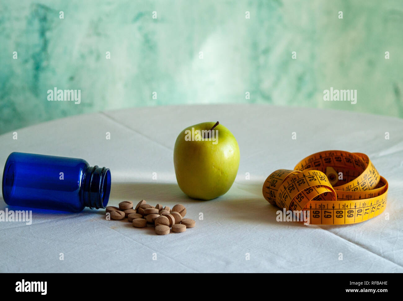 An apple, a tape measure and a blue container with vegetable fiber pills on a table Stock Photo