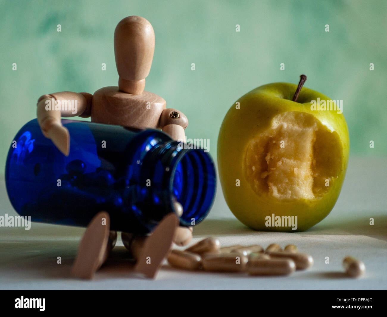 A wooden figurine with a bitten apple and a blue container with vegetable fiber pills on a table Stock Photo