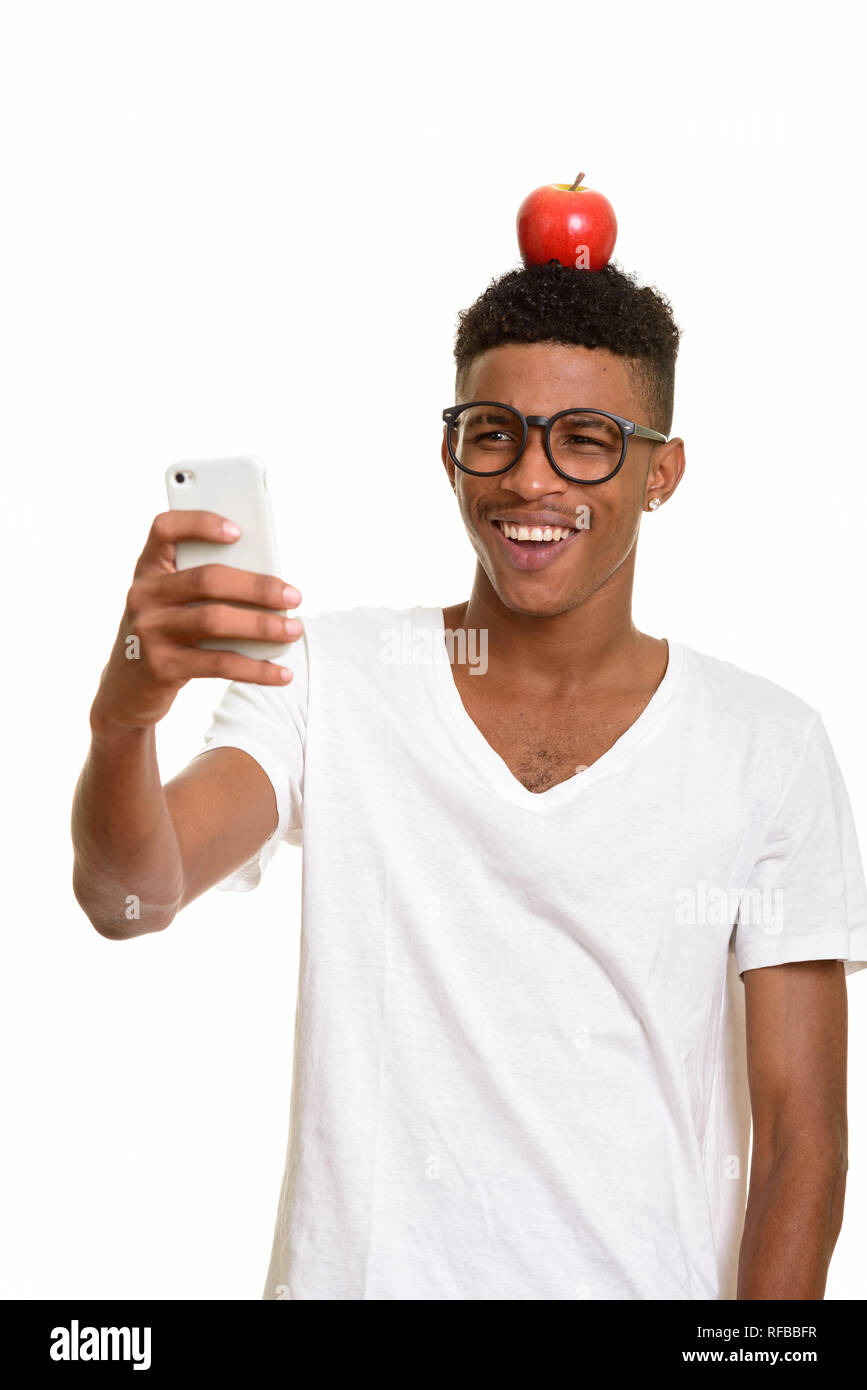 Young happy African man with apple on head while taking selfie Stock Photo