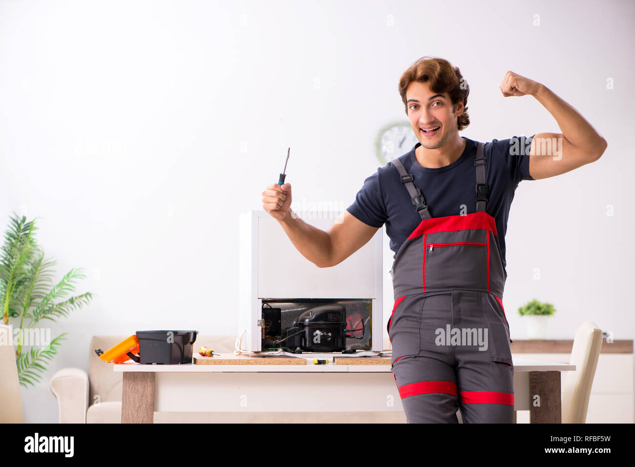 Young handsome contractor repairing fridge Stock Photo