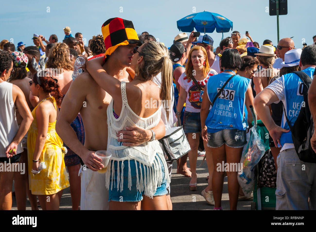 RIO DE JANEIRO, BRAZIL - FEBRUARY 18, 2017: A young Brazilian couple kisses in the middle of the crowd during a sunset Carnival bloco street party. Stock Photo