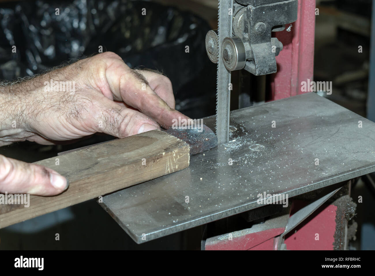 The metal worker carefully shapes a metal piece using a band saw for cutting. A bokeh background was captured. Stock Photo
