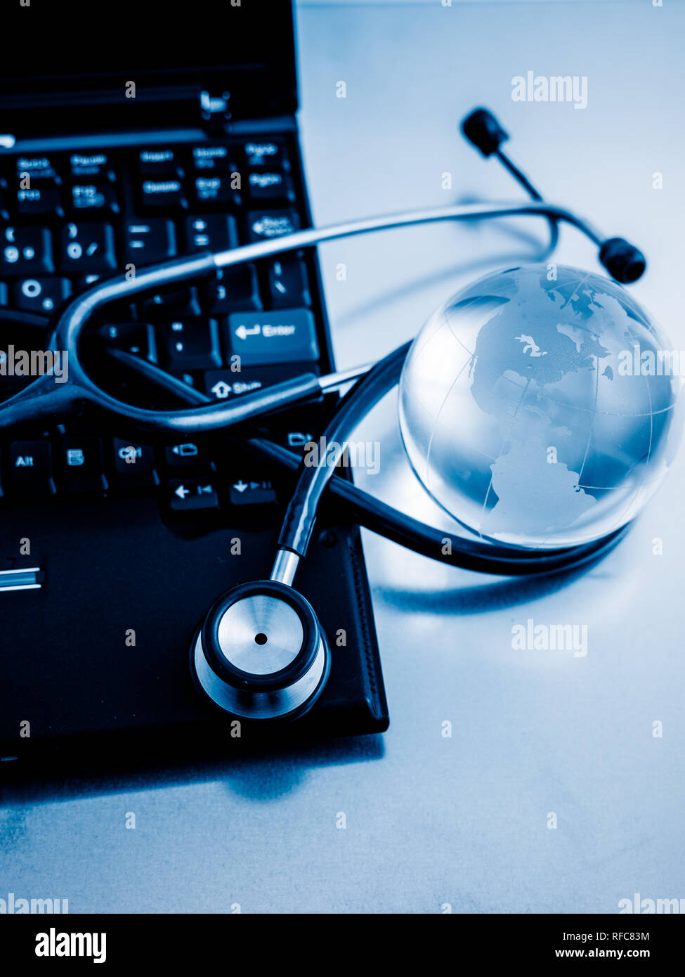 Glass globe and stethoscope on a computer keyboard.blue toned images ...