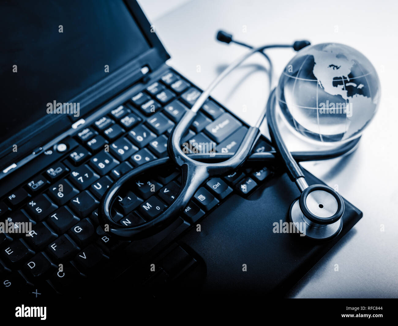 Glass globe and stethoscope on a computer keyboard.blue toned images ...