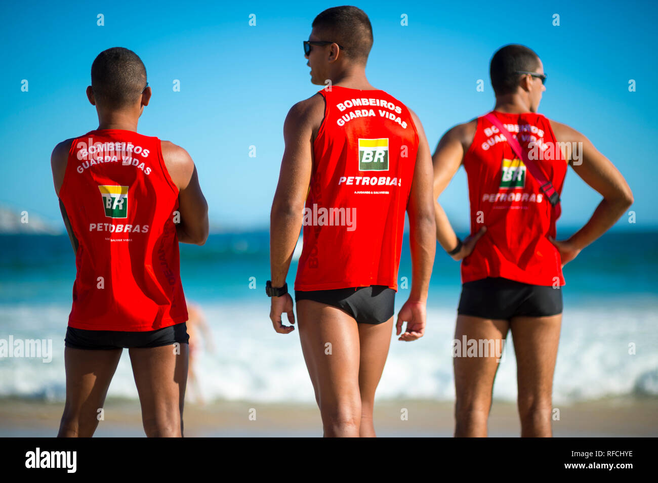 RIO DE JANEIRO - MARCH, 2018: A trio of Brazilian lifeguards in uniforms sponsored by embattled oil company Petrobras monitor surf on Ipanema Beach. Stock Photo