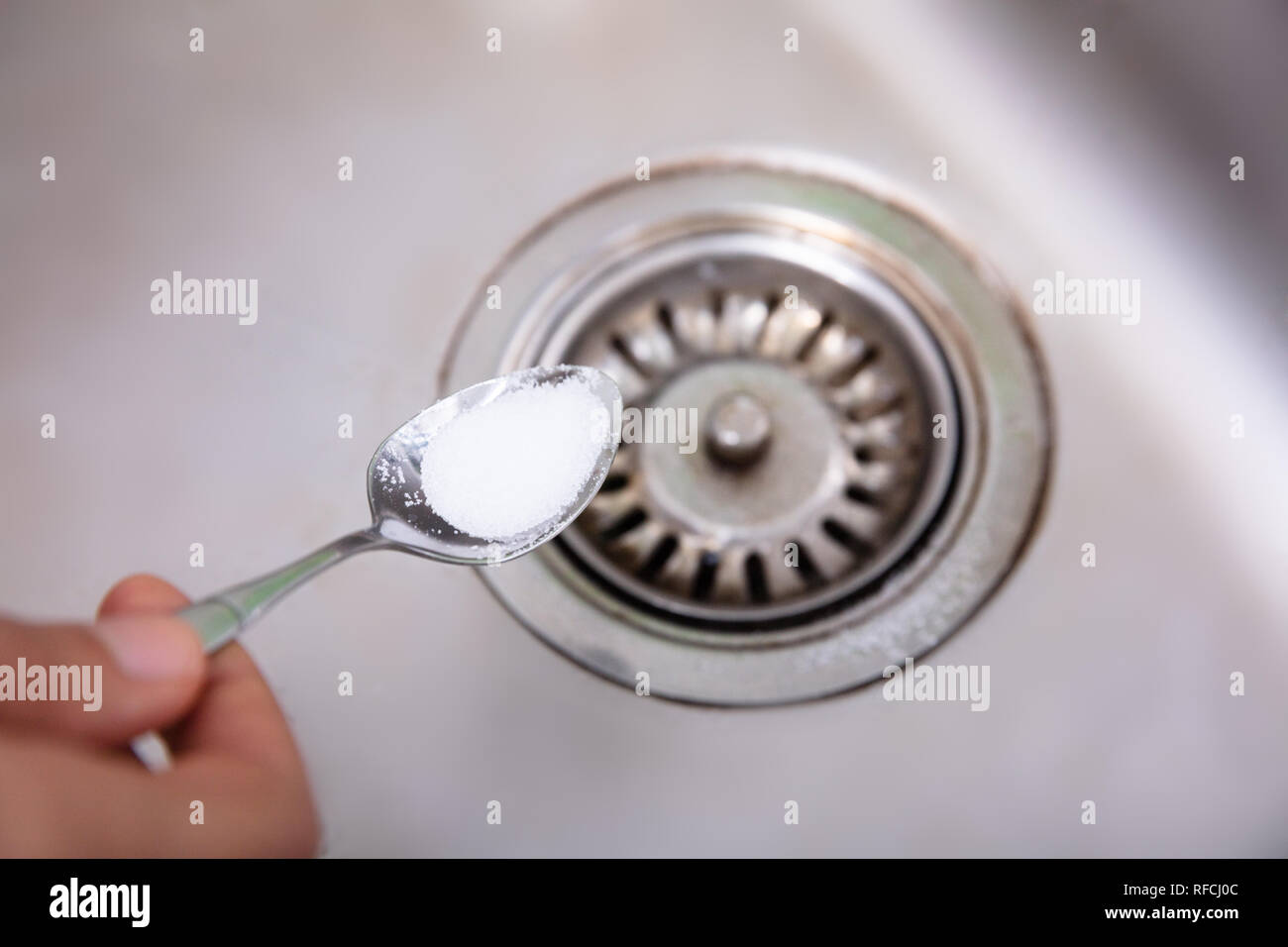 A Person Putting The Baking Soda With Spoon On Drain In The Washbasin