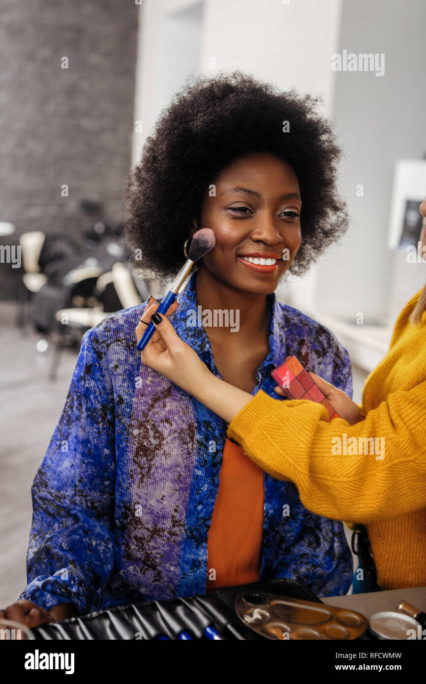 Pretty beaming dark-eyed model with curly hair smiling pleasantly Stock Photo