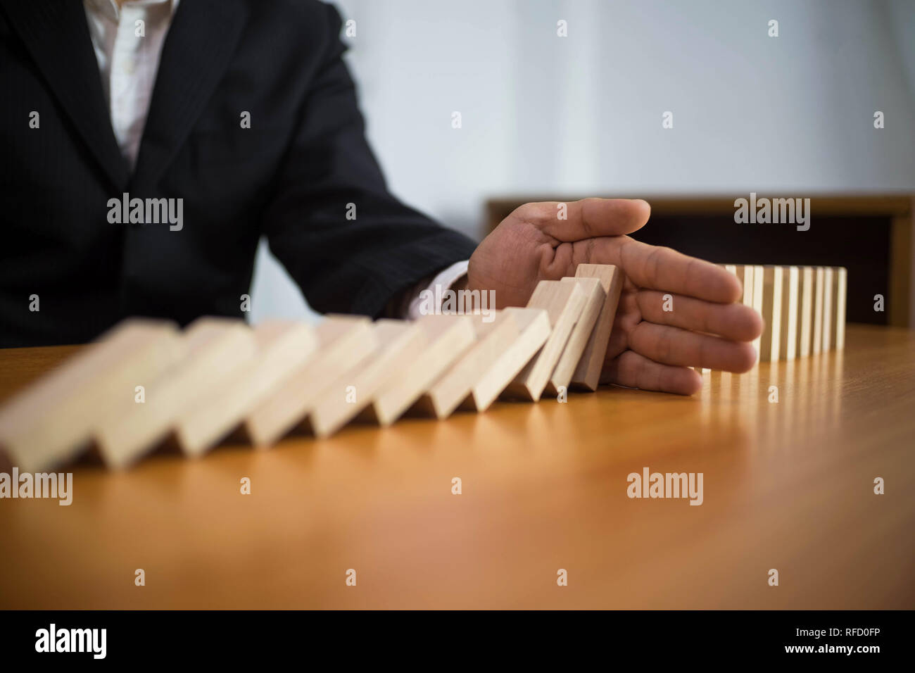 Businessman hand stops domino continuous overturned meaning that hindered business failure. Stop over this business failure concept. Stock Photo