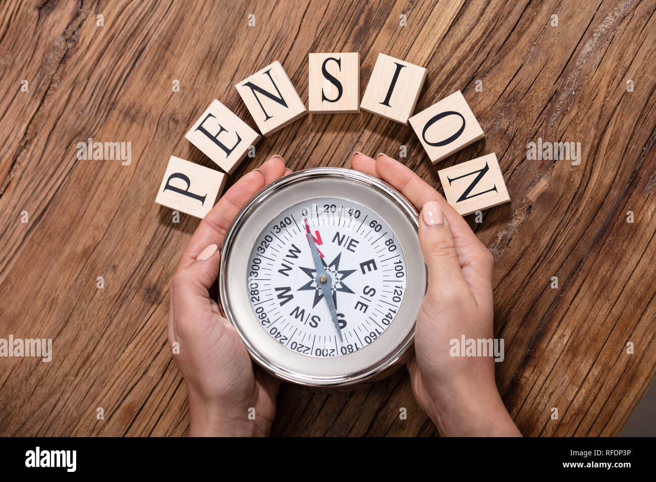 Close-up Of A Hand Holding Magnetic Compass In Front Of Pension Blocks Over The Desk Stock Photo