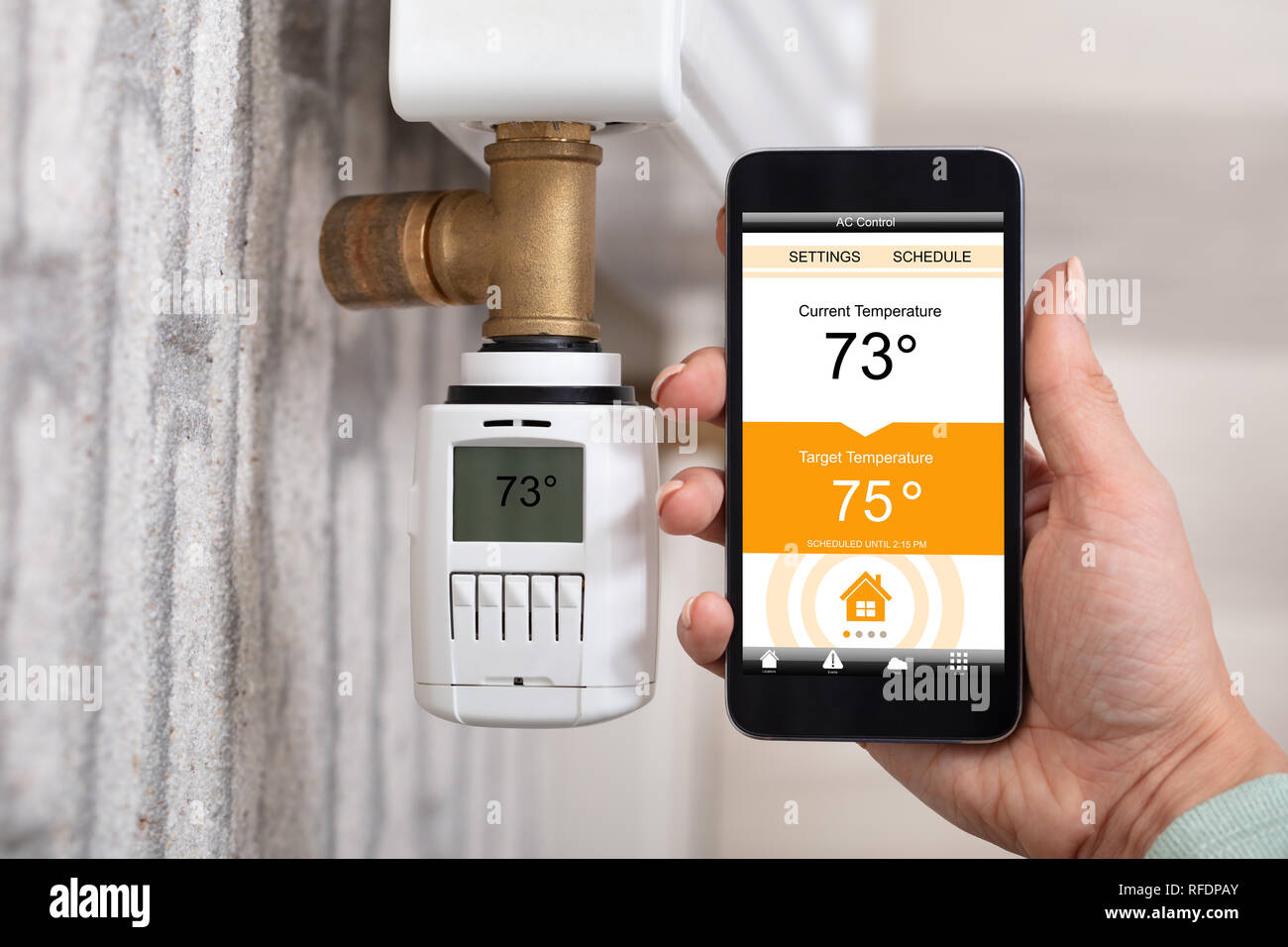 Close-up Of Person's Hand Adjusting Temperature Of Thermostat Using Cellphone At Home Stock Photo