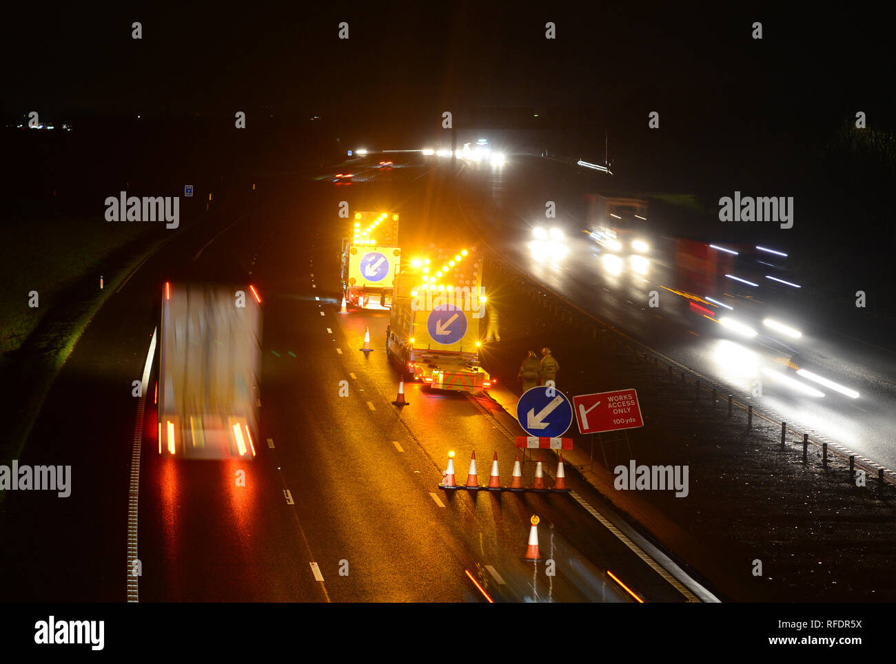 road workers with warning vehicles with flashing arrows closing lane at roadworks on the A1/m motorway at night leeds united kingdom Stock Photo