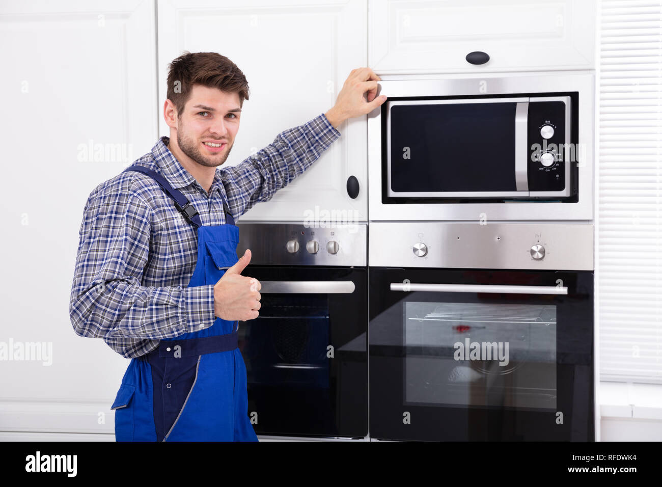 Portrait Of Technician Gesturing Thumb Up Standing In Front Of Microwave Oven Stock Photo Alamy