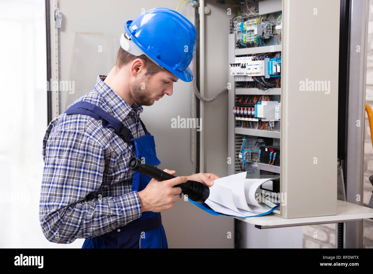Close-up Of Male Technician Holding Flashlight And Folder File In Front Of Fuse Box Stock Photo