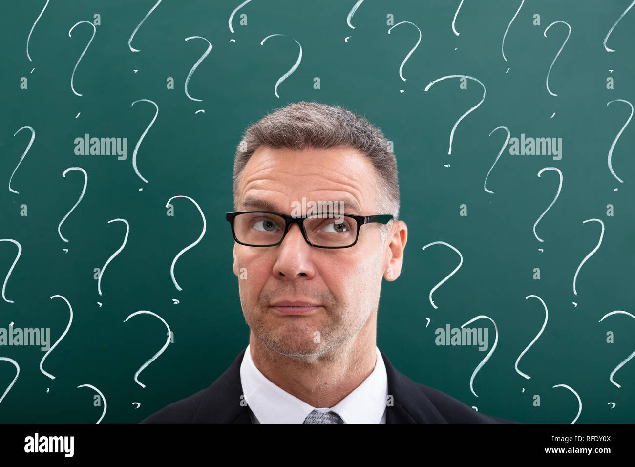 Thinking Mature Man In Front Of Question Marks Drawn On Chalkboard Stock Photo