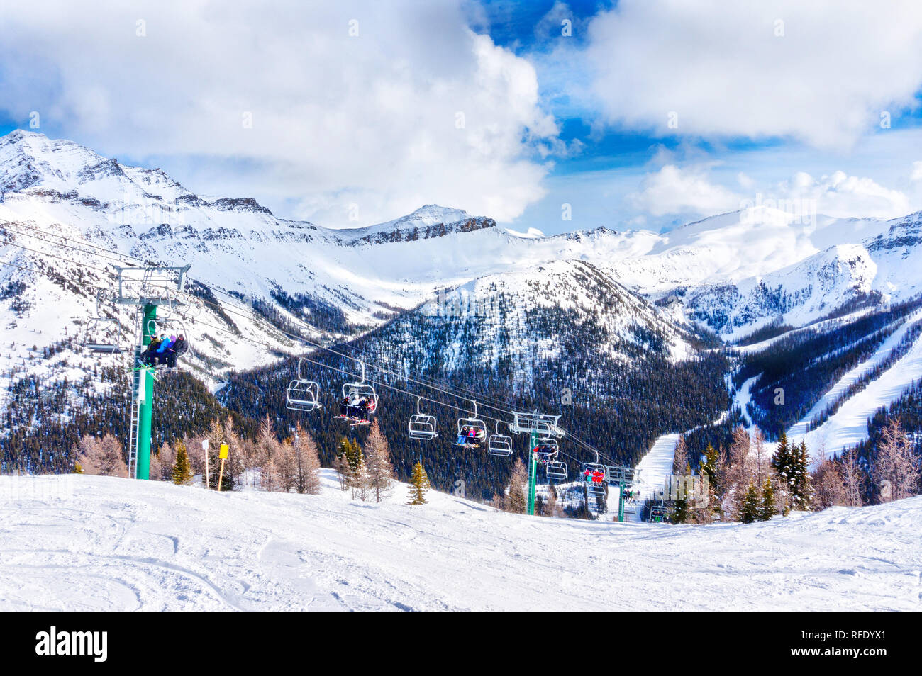 Unidentifiable skiers and snowboarders on chairlift going up a ski slope in the snowy mountain range of the Canadian Rockies. Stock Photo