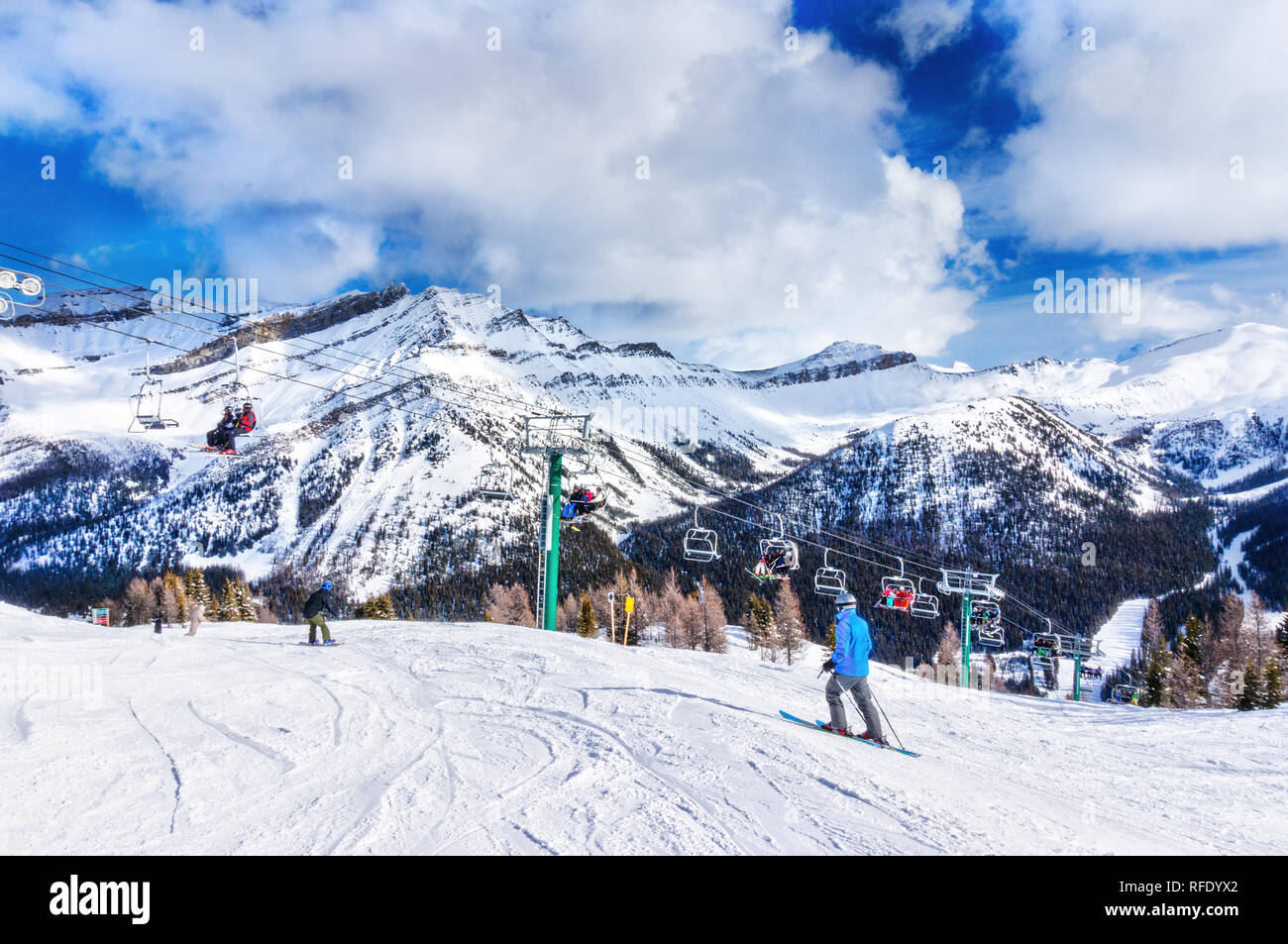Unidentifiable skiers and snowboarders on chairlift going up a ski slope in the snowy mountain range of the Canadian Rockies. Stock Photo